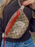 A close-up of a person wearing a beige GG Supreme canvas fanny pack with a bright orange-red leather zipper and a large white 'THE NORTH FACE' logo on the front.