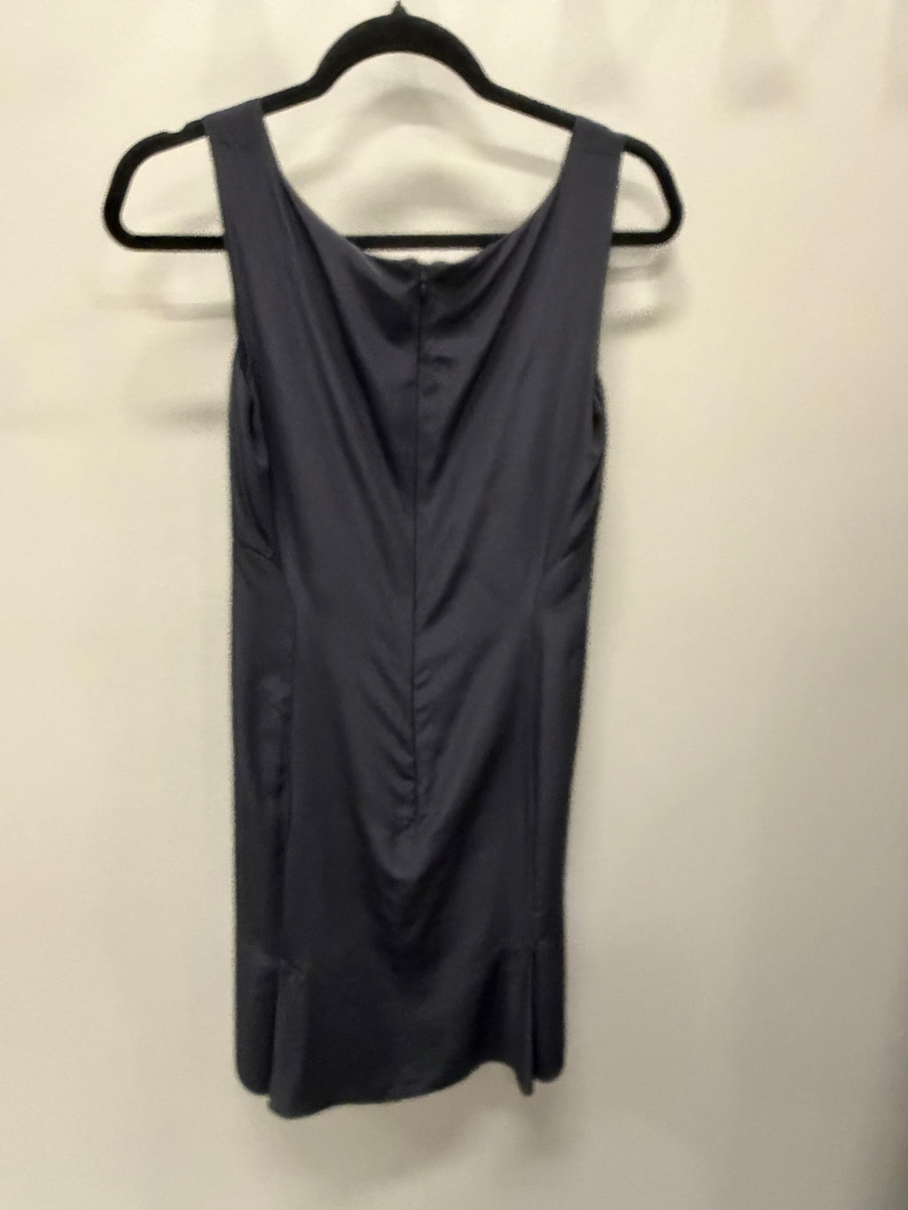 A sleeveless dark gray dress with a draped neckline and front ruching, hanging on a black hanger against a plain off-white wall.