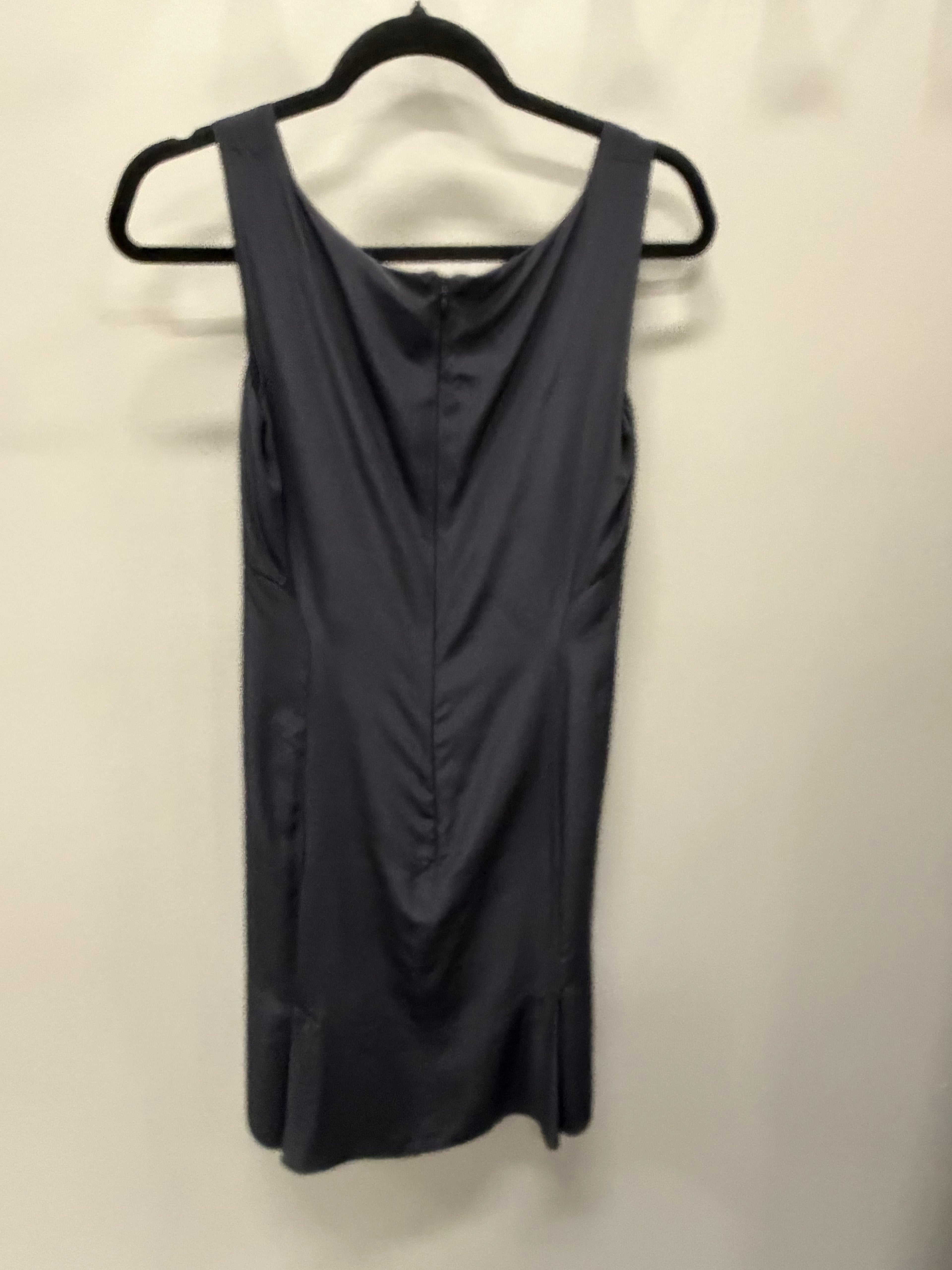 A sleeveless dark gray dress with a draped neckline and front ruching, hanging on a black hanger against a plain off-white wall.