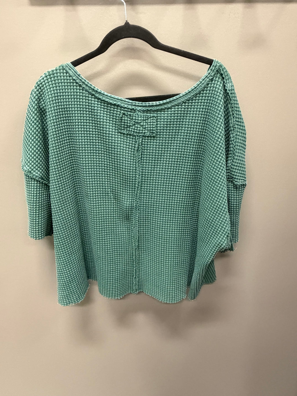 A green and white micro-check patterned blouse with a bow detail at the neckline, hanging on a black hanger against a plain beige wall.