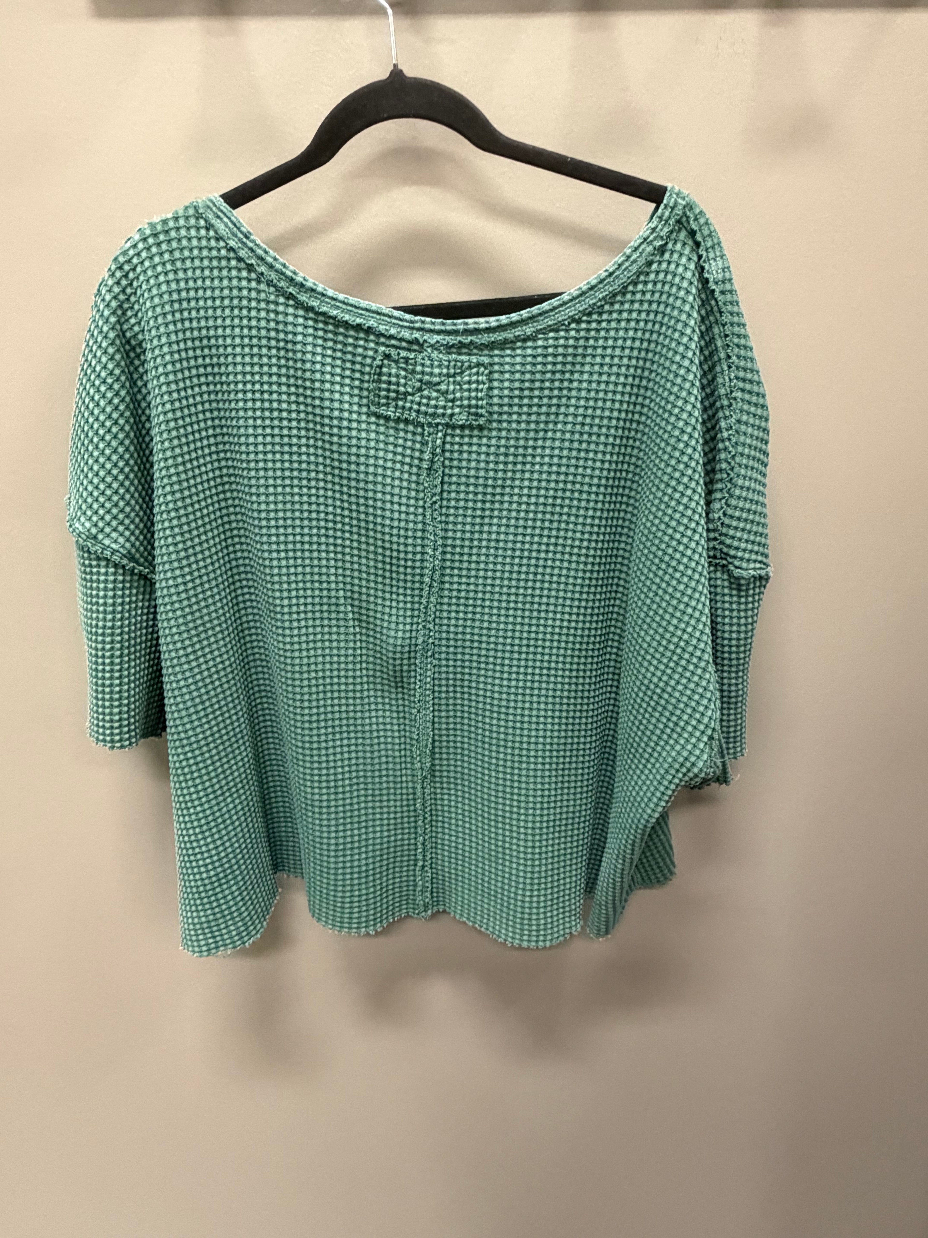 A green and white micro-check patterned blouse with a bow detail at the neckline, hanging on a black hanger against a plain beige wall.