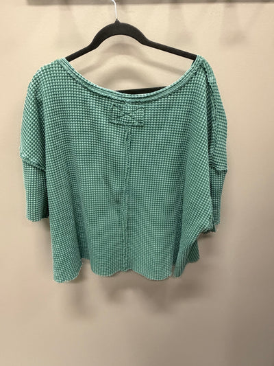 A green and white micro-check patterned blouse with a bow detail at the neckline, hanging on a black hanger against a plain beige wall.