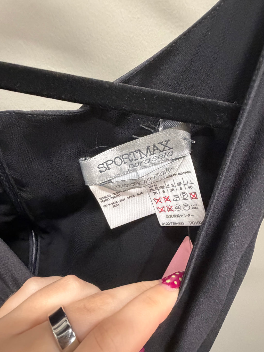 Close-up of the interior neck label of a black garment, showing the brand SPORTMAX by asolo and care instructions, with a person's fingers holding the label open.