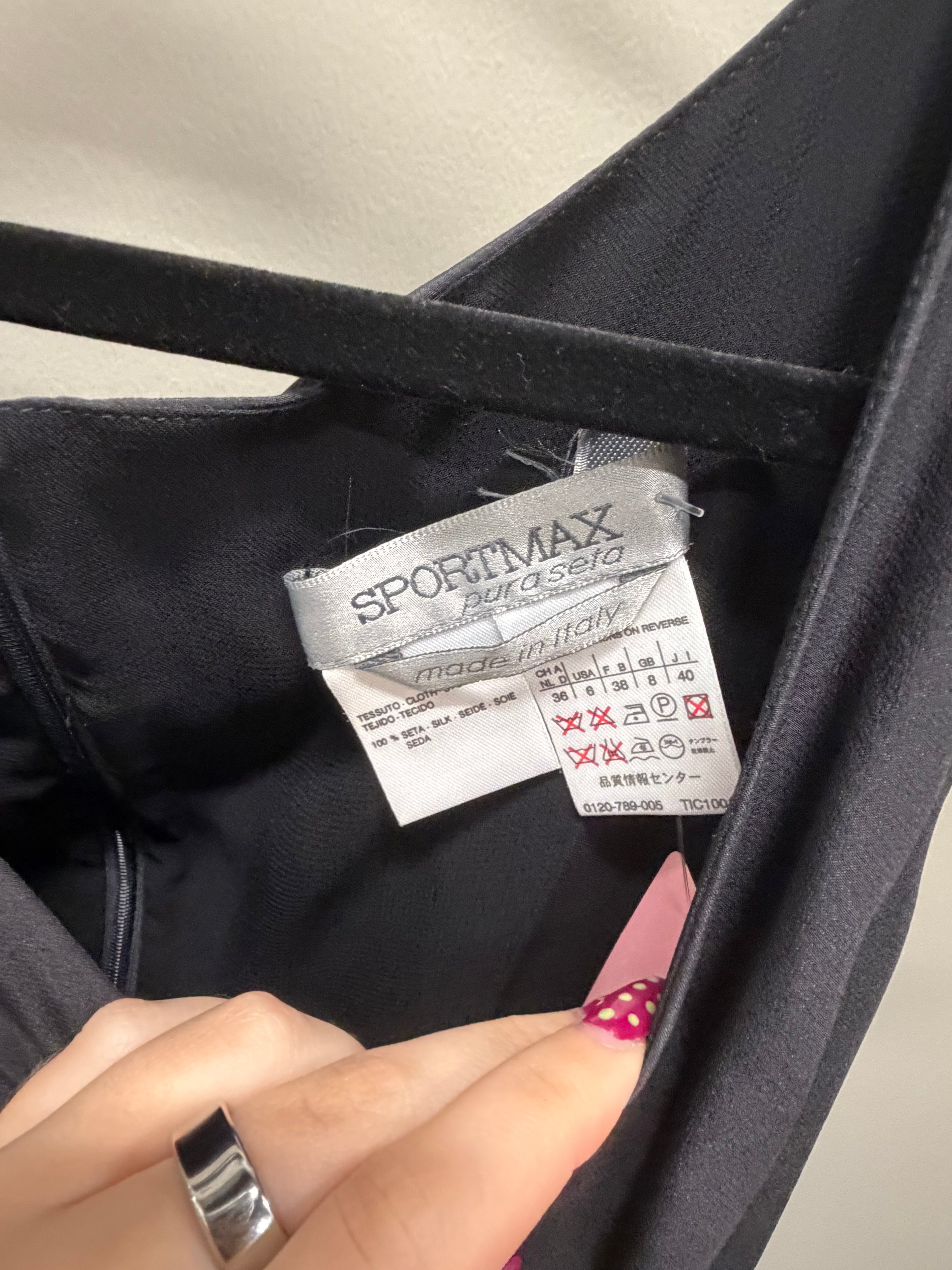 Close-up of the interior neck label of a black garment, showing the brand SPORTMAX by asolo and care instructions, with a person's fingers holding the label open.