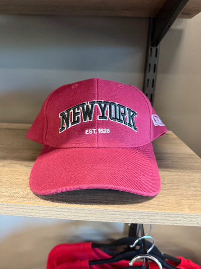 A pink baseball cap with 'NEWYORK EST. 1626' embroidered on the front, resting on a wooden shelf.