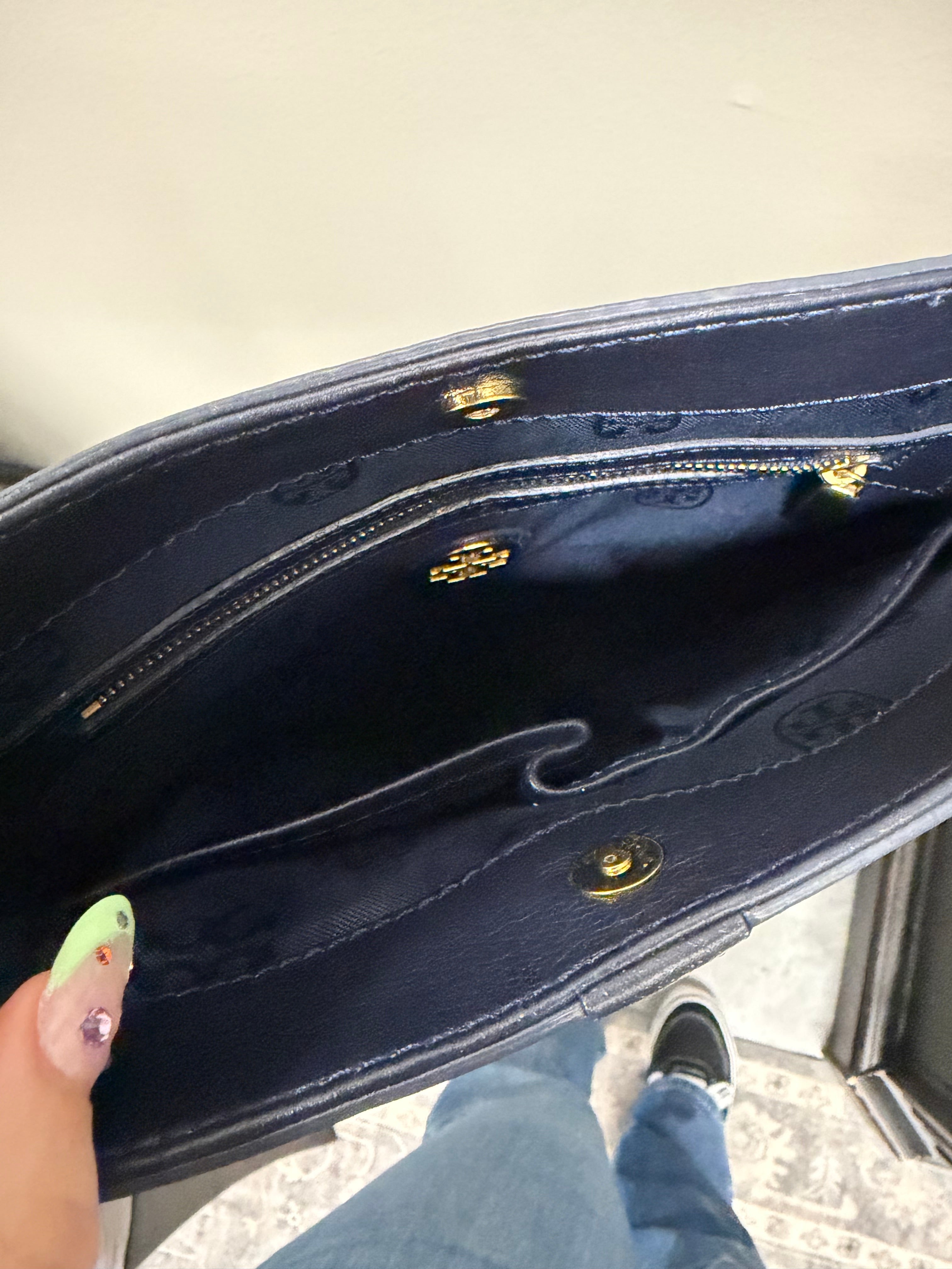Close-up of a dark blue handbag with gold accents on a light gray surface.