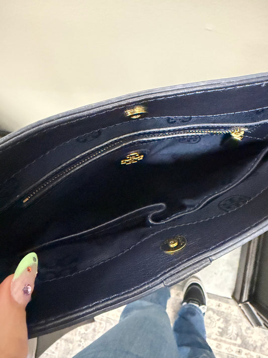 Close-up of a dark blue handbag with gold accents on a light gray surface.