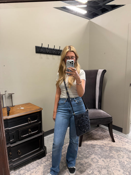 Person taking a mirror selfie wearing a white t-shirt and blue jeans in a room with a chair and dresser.