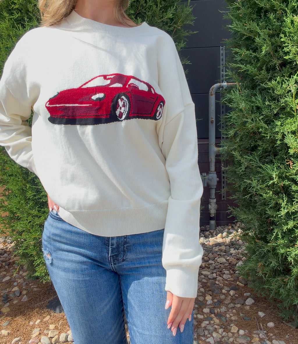 Person wearing a white sweatshirt with a red car graphic outdoors.