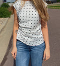 Person wearing a white t-shirt with black polka dots and blue jeans on a sidewalk.