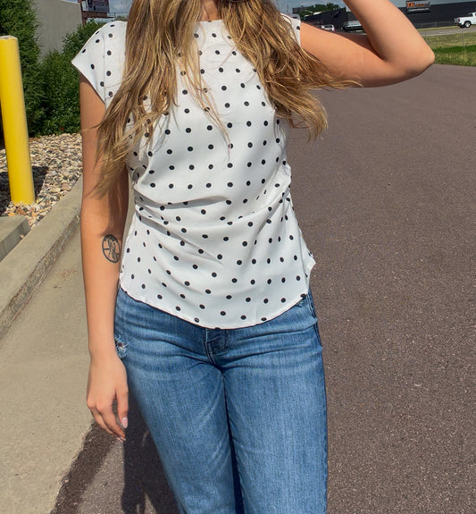 Person wearing a white polka dot top and blue jeans on a street.