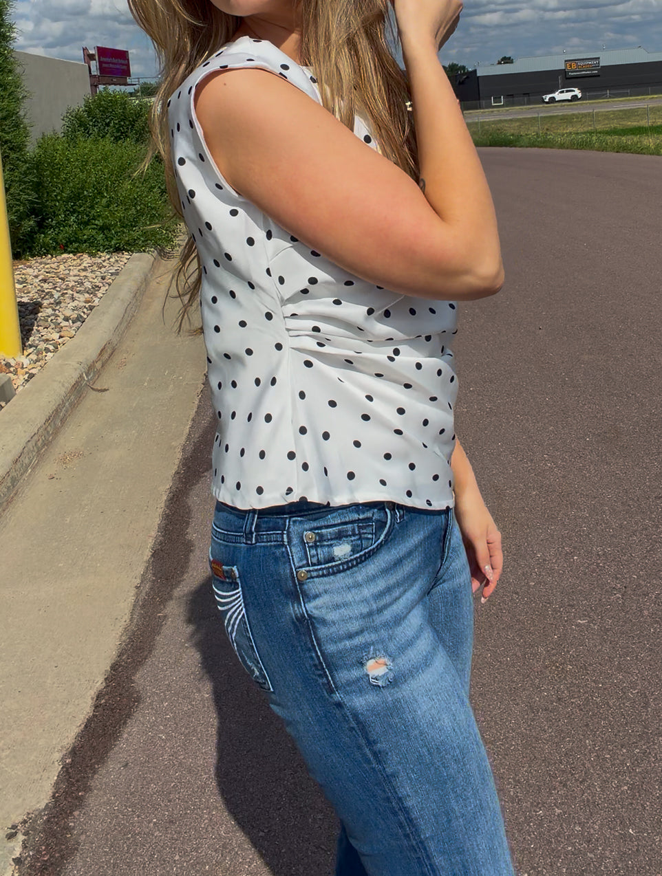 Person wearing a polka dot sleeveless top and blue jeans on a road.