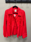 A bright red utility jacket hanging on a black hanger against a light gray wall. The jacket has a pointed collar, long sleeves, and front button closure, with a visible white retail price tag and a brand label inside the collar.