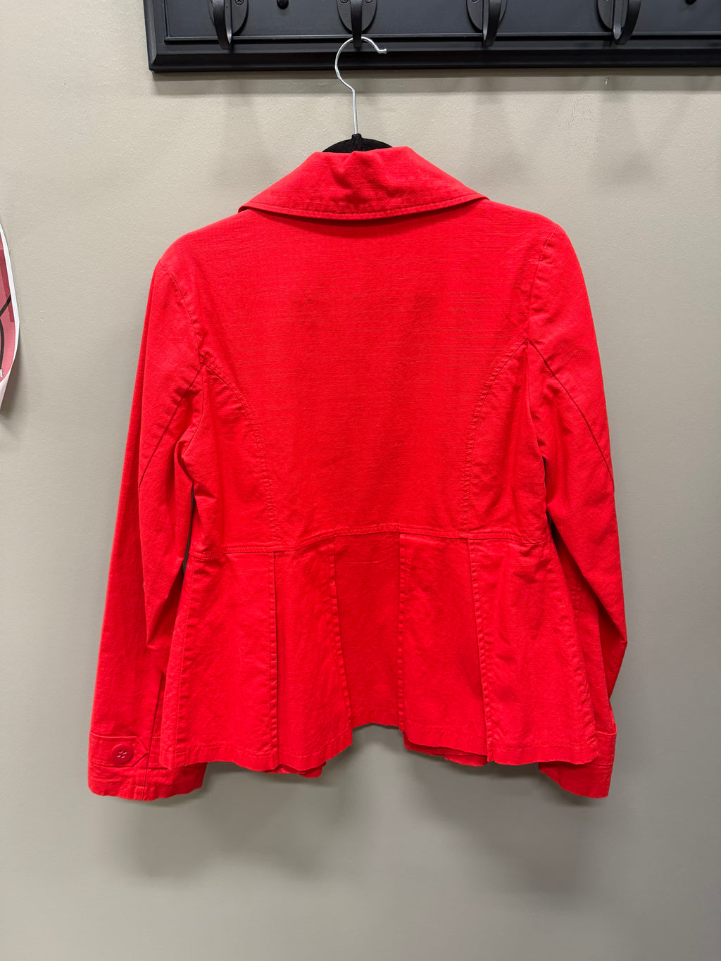 A bright red long-sleeve jacket hanging on a black hanger against a plain gray wall.