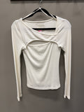 A white long-sleeve ribbed knit top with a unique cutout design on the chest, hanging on a black hanger against a dark gray wall.