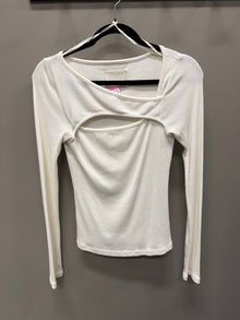 A white long-sleeve ribbed knit top with a unique cutout design on the chest, hanging on a black hanger against a dark gray wall.