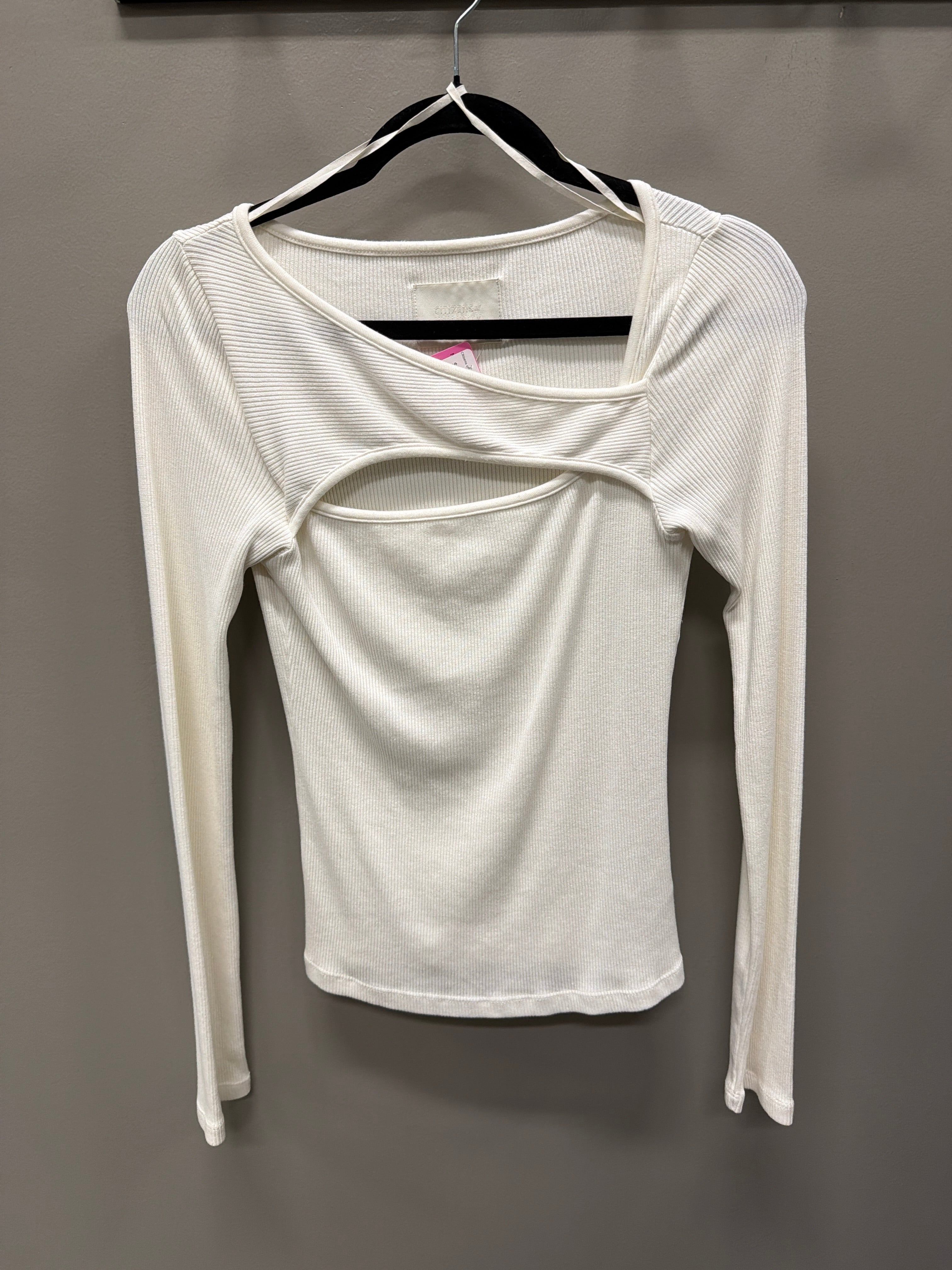 A white long-sleeve ribbed knit top with a unique cutout design on the chest, hanging on a black hanger against a dark gray wall.